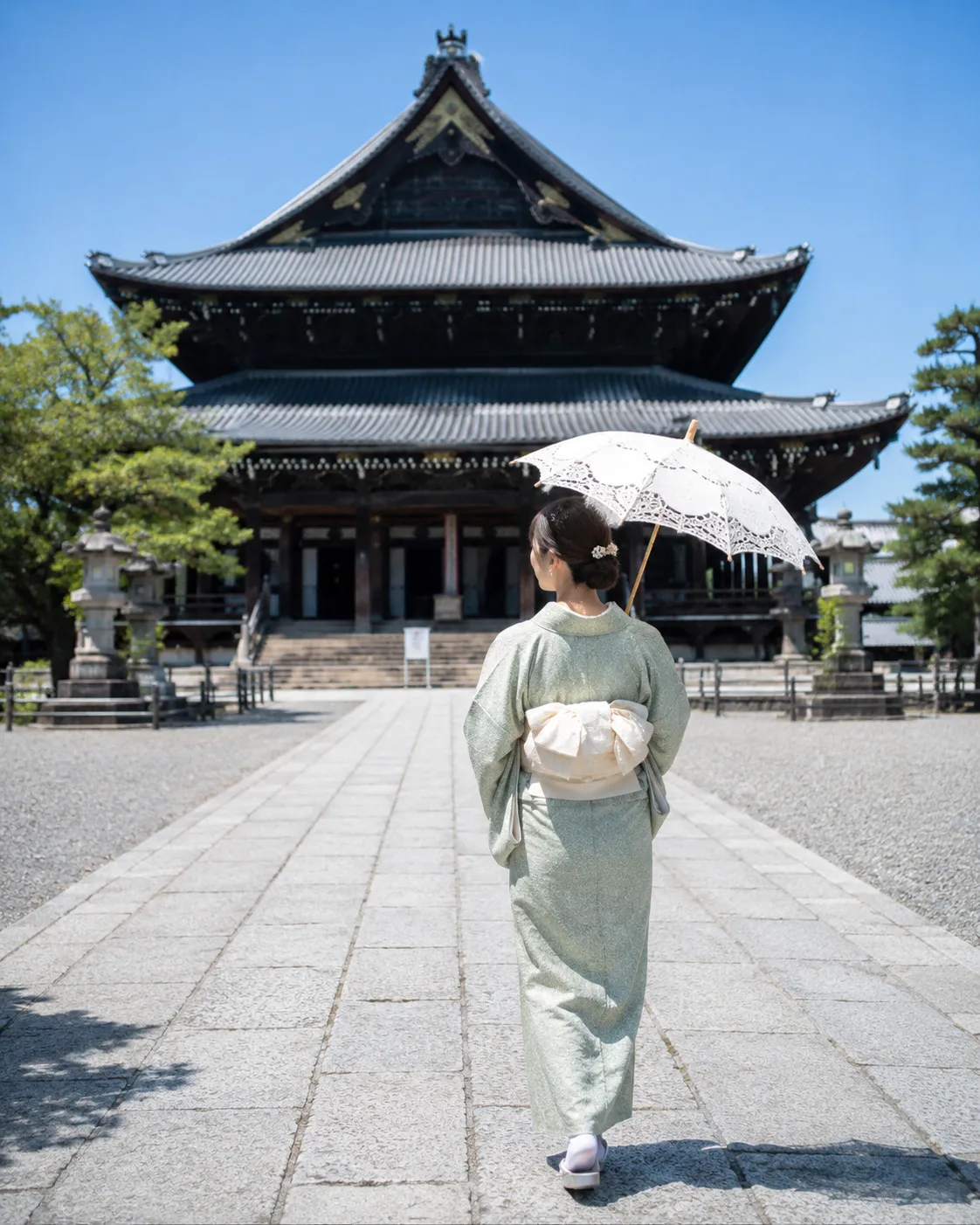 寺院の境内をレースの日傘を差して歩く着物姿の女性