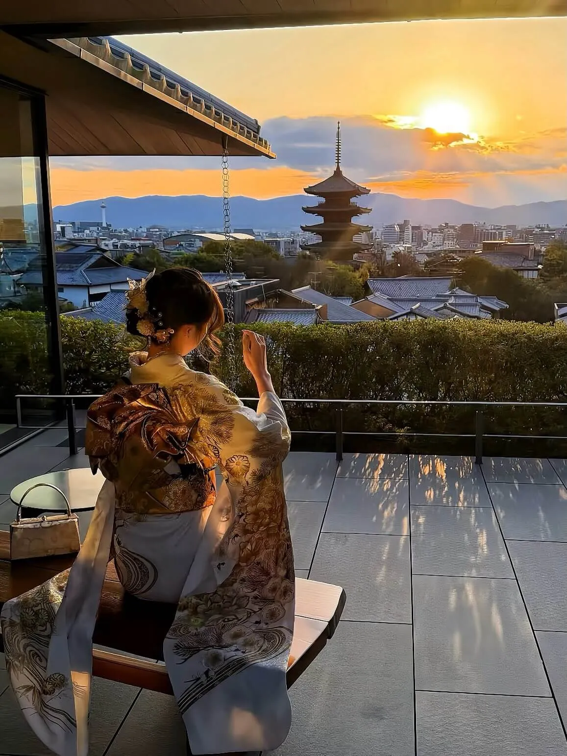 Woman in kimono seated on a terrace overlooking the five-story pagoda at dusk